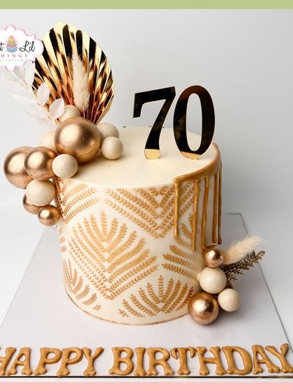 An elegant 70th birthday cake with a bohemian flair. This design features a stenciled gold pattern, dried botanicals, and a cascade of gold and white spheres.