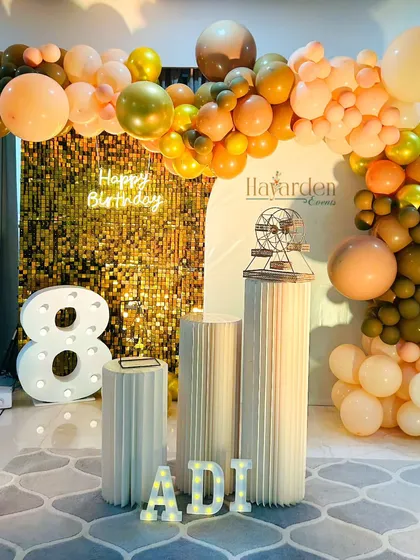 An elegant 18th birthday party. The decor features a half-arch of balloons in earthy tones, a gold sequin backdrop, and large marquee numbers.