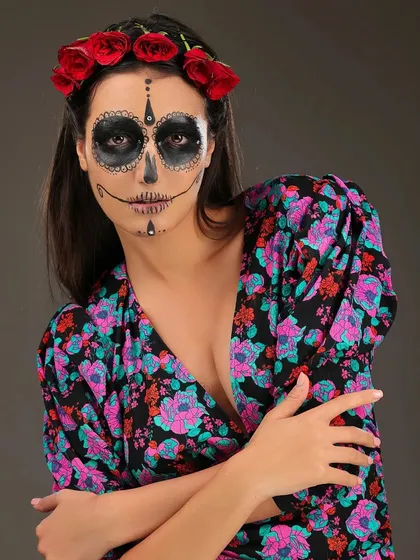 A Halloween-themed portrait of a model with "Day of the Dead" sugar skull makeup, wearing a floral dress and a red rose crown.