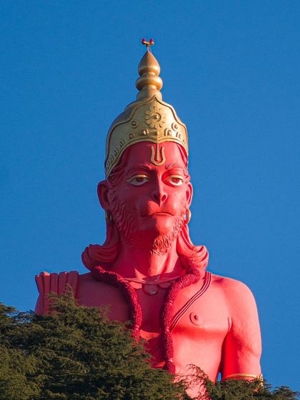 The towering 108-foot statue of Lord Hanuman at Jakhu Temple in Shimla, seen rising above the treetops against a clear blue sky.