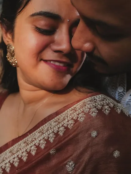 A beautiful close-up shot capturing the intricate details of her saree and the soft, intimate moment between the couple. The warm lighting adds to the romantic feel.