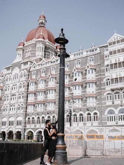 A long shot showing the couple in a quiet moment against the vast backdrop of the Taj hotel. This composition highlights the contrast between their intimacy and the grand scale of the city.