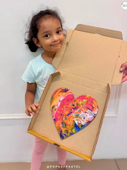 A close-up of this little artist's colorful, heart-shaped acrylic pour painting, ready to be taken home and treasured.