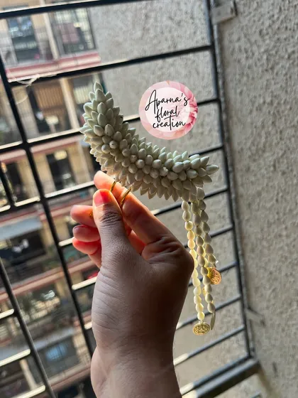 A 'Chandrakor' style hair pin, shaped like a crescent moon. This delicate accessory is made from jasmine buds and is a beautiful addition to a traditional hairstyle.