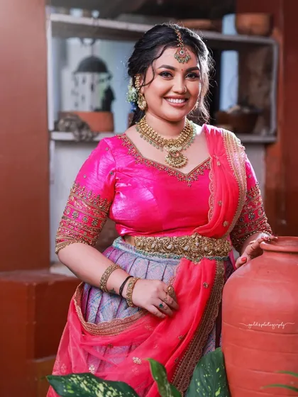 A bright and cheerful portrait. The vibrant pink of the half-saree and the bride's radiant smile create a joyful and celebratory mood.