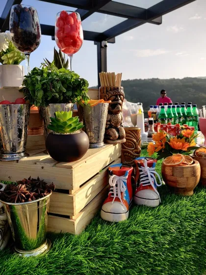 A quirky and fun setup for a garden party. This bar features tiki-style mugs and unique sneaker-shaped shot glasses alongside fresh garnishes like star anise, adding a playful touch to the outdoor setting.