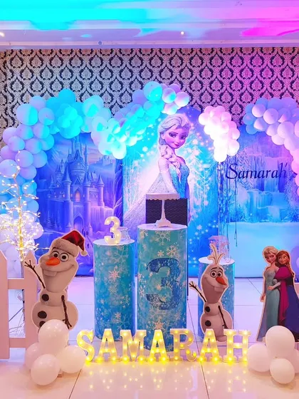We bring the magic of Arendelle to life with this Disney's Frozen theme decoration. The backdrop features Elsa's ice castle, surrounded by a balloon arch in shades of icy blue and white, with life-size cutouts of Anna, Elsa, and Olaf.
