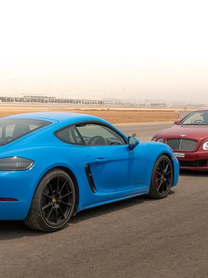 This shot focuses on the distinct rear designs of a modern Porsche Cayman and a luxurious Bentley Continental GT, side-by-side on the runway.