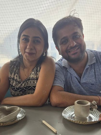 The proud creators with their finished, unpainted pieces. This couple is all smiles, showcasing the heart-shaped bowl and mug they made together during their pottery date.