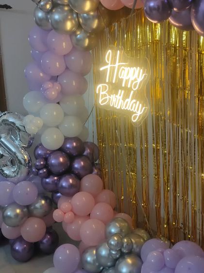 Celebrating a 28th birthday with a lush balloon arrangement in shades of purple, pink, and silver, complete with a foil number balloon and a neon sign.