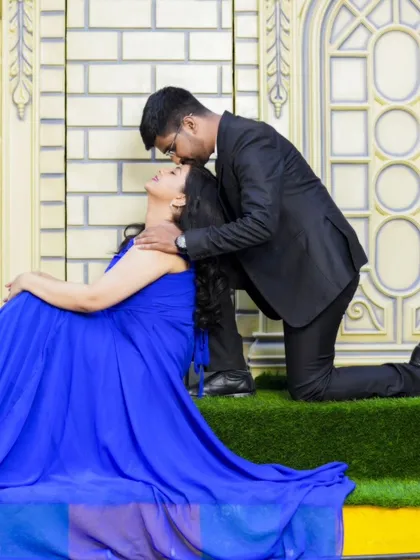 A tender moment with the groom kissing the bride's forehead. Her elegant blue gown and the beautiful indoor set create a romantic atmosphere.