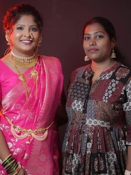 A student proudly stands next to her model, who is styled in a lovely pink saree for a party or engagement look.