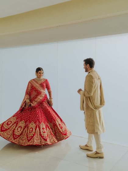 The bride twirls in her vibrant red lehenga, creating a beautiful motion shot. The clean, minimalist background allows her joyful movement and stunning outfit to be the main focus.