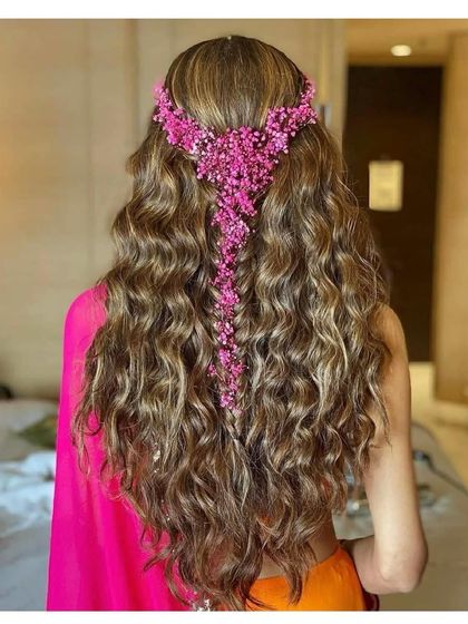A stunning hairstyle for long hair, perfect for a Mehendi or Sangeet. We created beachy waves and added a beautiful pink floral hair accessory that cascades down the braid.