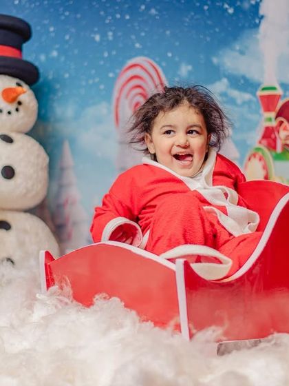 Pure holiday joy! A toddler in a Santa suit laughs with delight while sitting in a sleigh, part of my special Christmas mini-sessions.