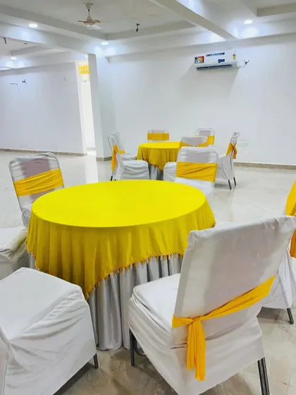 Simple and clean guest seating for a Haldi function. I provided round tables with yellow tablecloths and chairs with white covers and matching yellow sashes.