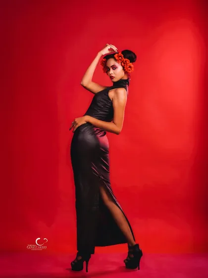 A dramatic and artistic pose in a black leather dress, accented with red flowers. The red background creates a powerful, monochromatic color story.