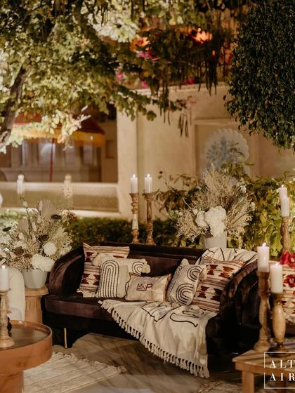 A comfortable lounge area at the 'Muted Melodies' sangeet, with textured pillows and warm throws under a canopy of trees. The design was meant to feel like a cozy, contemporary, and luxurious escape.