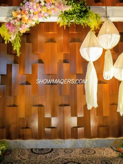 A unique photo backdrop featuring a textured wooden wall, modern fabric lanterns, and asymmetrical floral arrangements. This design combines rustic and contemporary elements for a stylish look.
