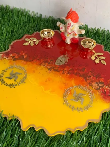 A festive pooja platter in auspicious shades of red and yellow, featuring swastika symbols and holders for diyas or kumkum.