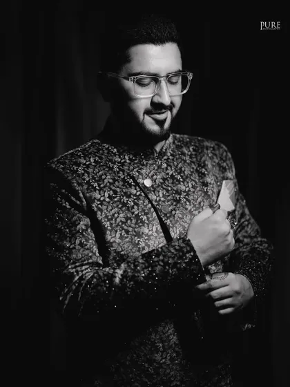 A dapper black and white portrait of the groom-to-be, looking sharp in his patterned bandhgala.