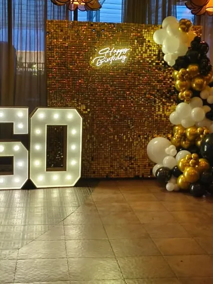 I make milestone birthdays like a 50th truly shine. This setup features a dazzling gold sequin shimmer wall, a custom "Happy Birthday" neon sign, and large, bright light-up marquee numbers that create the perfect photo opportunity.