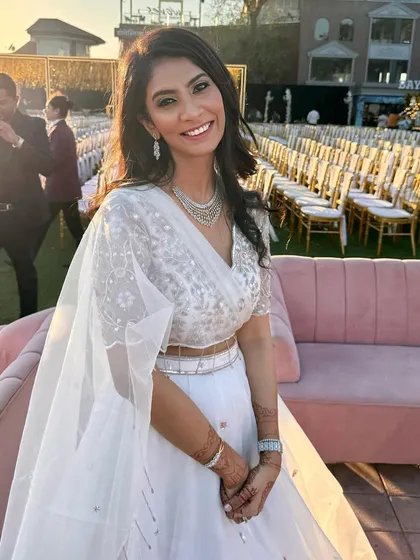 A happy guest at an outdoor wedding. The makeup is designed to look great in natural sunlight, with a focus on a fresh base and a bright, welcoming smile.