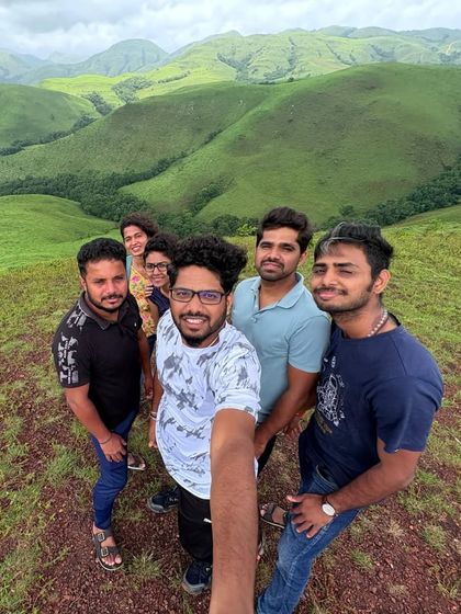A wide-angle selfie capturing the happy faces of the group and the stunning green landscape of Kudremukha behind them.