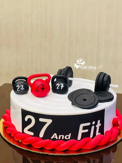 A '27 and Fit' cake for a gym enthusiast. The cake is topped with edible, handcrafted fondant weights, kettlebells, and a barbell, perfect for a fitness lover's birthday.