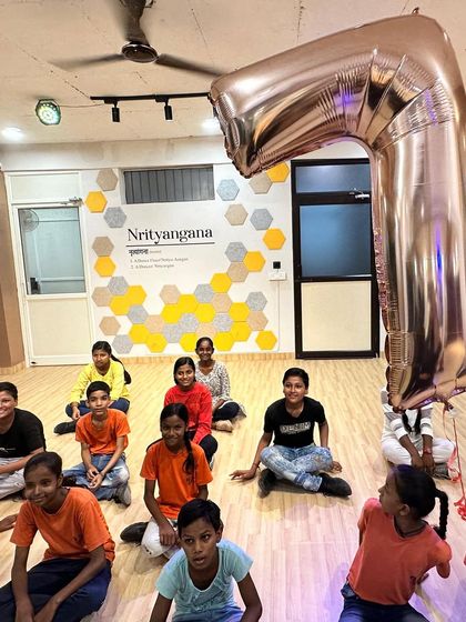 The children from the NGO sitting on the floor of our studio, with a large '7' balloon from our anniversary celebration.