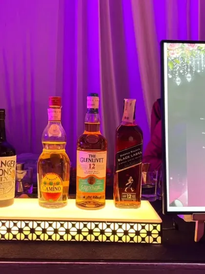 A clean and modern bar display featuring a backlit platform for premium spirits like The Glenlivet and Stranger & Sons gin. The illuminated menu board clearly lists the custom cocktails and mocktails available.