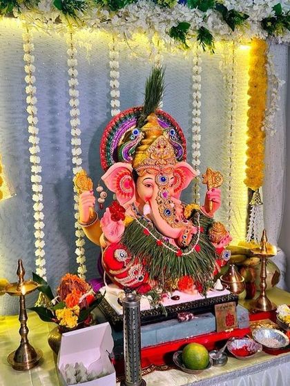 A traditional Ganpati setup with hanging garlands of marigolds and white flowers. The simple white backdrop is illuminated with lights, keeping the focus on the beautifully adorned idol.