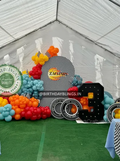 A race car party set up inside a tent, showing the versatility of the theme. The checkered backdrop and colorful balloons create a festive atmosphere.