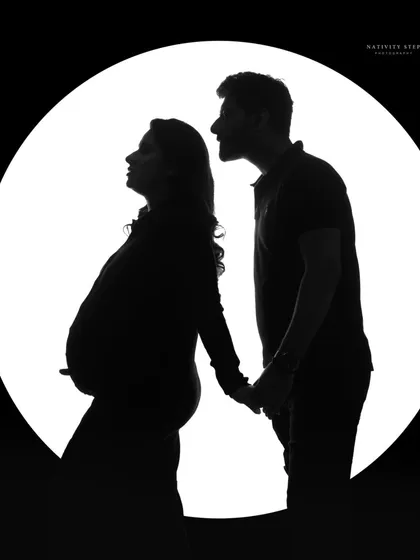 A classic couple's silhouette against a circular light source. This timeless black and white shot emphasizes their bond and the shape of the baby bump.