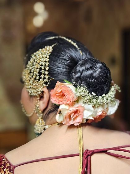 A detailed shot of the bridal bun, adorned with fresh flowers and a traditional hair accessory. The hairstyle is just as important as the makeup.