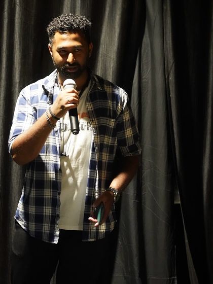A performer confidently holds the mic, addressing the audience during our open mic event. The simple black curtain backdrop ensures that all attention is on the artist.