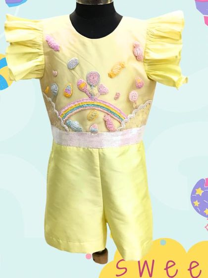 Our Candyland Playsuit is as sweet as it gets. The yellow playsuit features hand-embroidered candies and a rainbow on the bodice, making it a fun and practical choice for a play-area birthday.