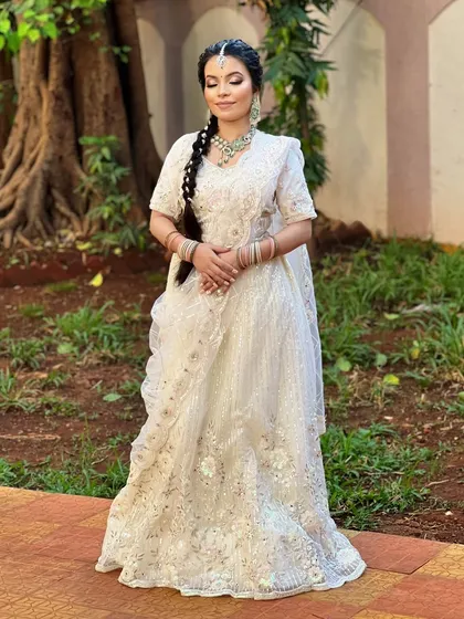 A full-length shot of the bride in her white lehenga, showcasing a unique braided hairstyle and the elegant, understated jewellery.