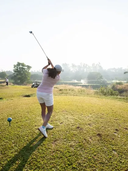 We welcome golfers of all levels and backgrounds. Here, a player is captured mid-swing, teeing off on a beautiful morning with the course's water features and lush landscape in the background.