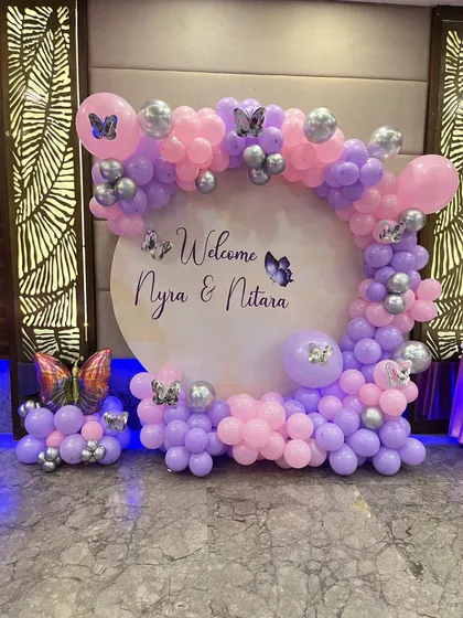 A welcome decoration with a butterfly theme. This setup features a circular backdrop with custom names and a balloon arch in purple and pink.