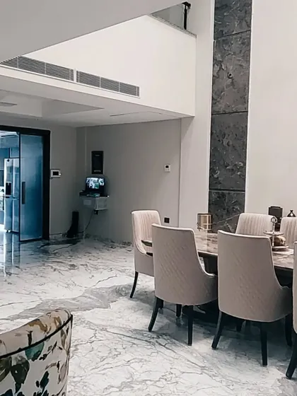 This photo from a completed Gurgaon residence showcases a double-height dining area with a dramatic stone-clad column. The polished marble flooring and minimalist furniture create a grand yet uncluttered atmosphere, reflecting my signature style.