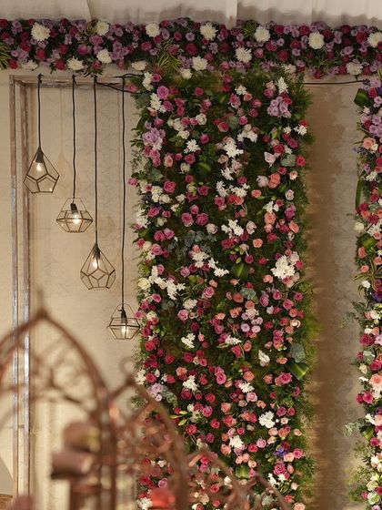 A detail shot of the floral wall, showing the mix of roses and other blooms, with modern geometric pendant lights hanging alongside.