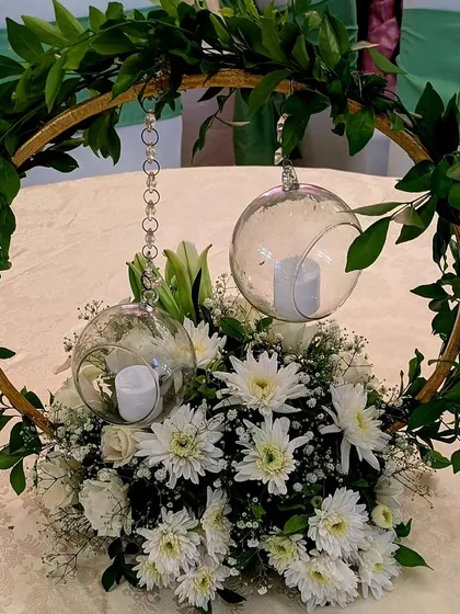 A modern and minimalist centerpiece, featuring a golden hoop with hanging glass orbs and candles, set within a bed of white chrysanthemums and baby's breath.