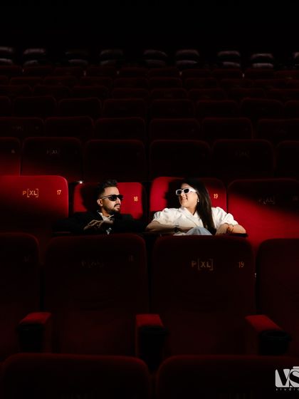 A cool, cinematic shot of a couple in an empty movie theatre. The dramatic red lighting and their stylish sunglasses give this pre-wedding photo a bold, movie-star vibe.
