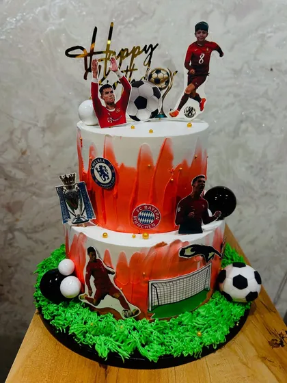A two-tier football-themed cake celebrating various clubs and players, perfect for a die-hard fan's birthday.
