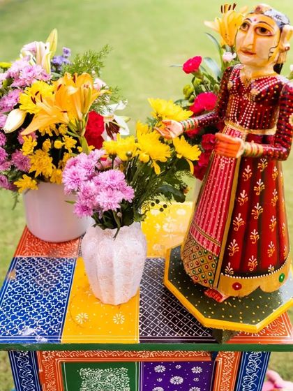 A hand-painted side table featuring a traditional Rajasthani doll and fresh flowers. These artistic details add a layer of authenticity and charm to a themed wedding event.