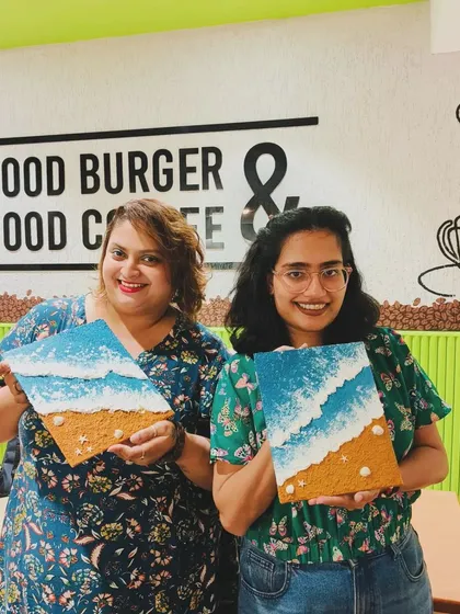 Two friends posing with their matching beach texture paintings. It's a great way to create something together and have a shared memory.