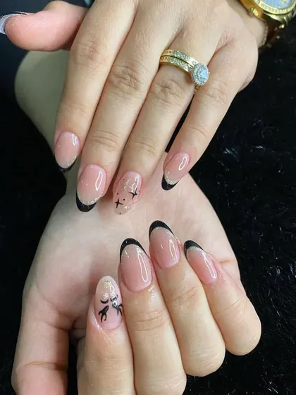 A playful French manicure with black tips on almond-shaped nails, featuring accent nails with delicate star and reindeer art.