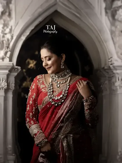 A beautifully framed shot of the bride in a traditional red saree. The architectural archway creates a perfect frame for this regal portrait.