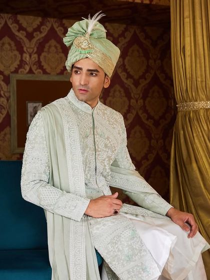 Posed against a rich backdrop, the pastel green sherwani stands out for its unique color and detailed craftsmanship, making it a memorable choice for any groom.